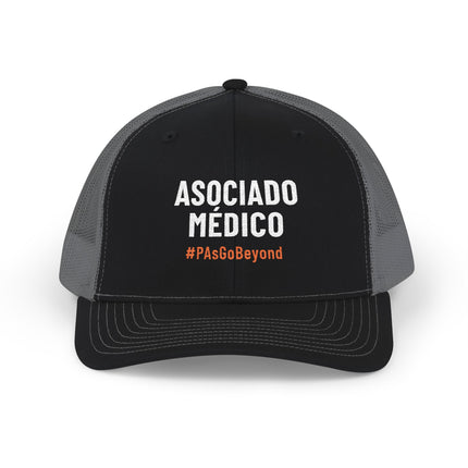 Black and grey trucker hat embroidered with "Asociado Médico" in white text and "#PAsGoBeyond" in orange.