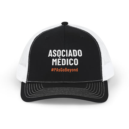 Black and white trucker hat embroidered with "Asociado Médico" in white text and "#PAsGoBeyond" in orange.