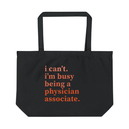 Black canvas tote bag printed with "i can't. i'm busy being a physician associate." in orange text.